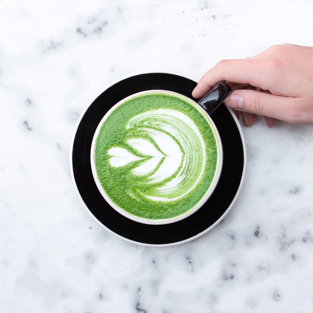 Top-down matcha latte with leaf latte art in a black cup